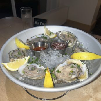 Nafsi - Oysters - Oysters served on ice with lemon wedges and two small containers of sauce, presented on a white platter. - New American Near Me - Chicago, Illinois
