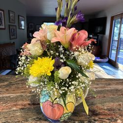 One of a Kind Floral Design - Purple gladiolus, coral lilies, white roses, yellow daisies in a water pitcher with baby's breath and greenery.