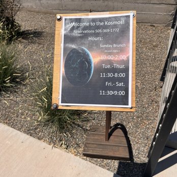 The Kosmos - Outdoor sign - An outdoor sign for The Kosmos restaurant shows hours for Sunday brunch and weekday hours, with reservation contact details. - Bars Near Me - Albuquerque, New Mexico