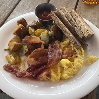 Sly Rooftop Bar - American breakfast, good size and tasty - A breakfast plate featuring scrambled eggs, crispy bacon, toasted bread, roasted potatoes with vegetables, and a small cup of ketchup on a white plate. - Breakfast & Brunch Near Me - Washington, DC, District of Columbia
