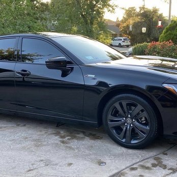 Premier Window Tinting - A black four-door sedan with tinted windows is parked on a concrete driveway next to a garage and some greenery. - Car Window Tinting Near Me - Lancaster, California