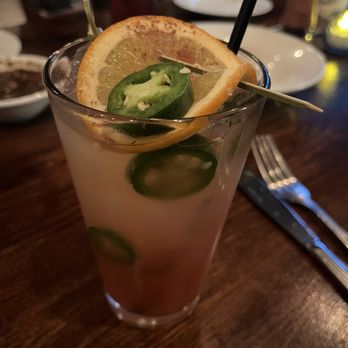 Charro Steak - The dry heat mocktail - A beverage in a tall glass is garnished with lemon and jalapeño slices, served with a straw, on a wooden table at a restaurant. - Steakhouses Near Me - Tucson, Arizona