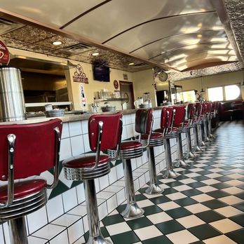 Gabby's Diner - Diner Seating / Ambiance - A classic diner interior featuring red vinyl bar stools with chrome accents, a tiled counter, and a checkered black-and-white floor. - American Near Me - Milan, New Mexico