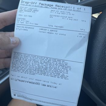 The UPS Store - Amazon Return - A paper receipt from UPS for a package drop-off, held by a person inside a vehicle. The receipt includes details such as the drop-off location at The UPS Store in Clovis, CA, the date and time of drop-off, estimated pickup date, package weight, and tracking reference. The background shows part of the vehicle's interior, including the steering wheel. - Printing Services Near Me - Clovis, California