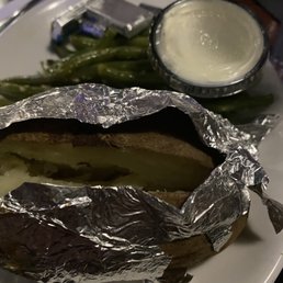 Prime rib sides: Baked potato and green beans "with" red peppers - A baked potato wrapped in aluminum foil, served with green beans and a small cup of creamy dipping sauce, on a plate.