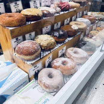 Union Square Donuts - A glass display case at Union Square Donuts in Boston shows an assortment of donuts, including glazed, frosted, and filled varieties, arranged on wooden trays. - Donuts Near Me - Boston, Massachusetts