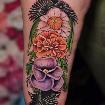 Jackalope Tattoo - A woman's inner forearm with a full color tattoo of a violet, marigold, and daffodil flowers surrounded by green leaves and 2 black crows. - Tattoo Near Me - Minneapolis, Minnesota