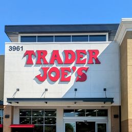 Trader Joe's grocery store exterior with a prominent sign, pumpkins displayed outside, and a clear entrance under a blue sky.