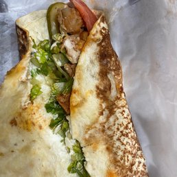 chicken - A folded flatbread with visible fillings of vegetables, meat, and pickles, served on parchment paper.