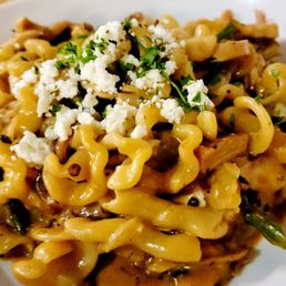 Chipotle Chicken Pasta - A close-up of a pasta dish featuring campanelle noodles mixed with pieces of chicken, topped with crumbled cheese and chopped herbs. The pasta appears coated in a sauce, and the dish is served in a white bowl, highlighting the textures and ingredients.