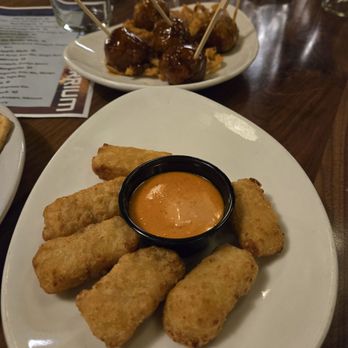 ENTERRIUM - mac bites and meatballs - Fried mozzarella sticks with a side of orange dipping sauce are arranged on a white plate at a restaurant table. - New American Near Me - Schaumburg, Illinois