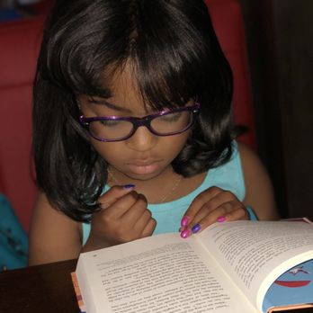 Hercules Library - In those books- no matter where or what - A girl with glasses and dark hair is reading a book at a table, with her hands resting on the pages. - Libraries Near Me - Hercules, California