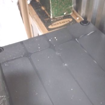Extra Space Storage - The image shows a black surface, likely a table or countertop, with visible dust and small debris scattered across it. Behind this surface, there is a cardboard box with a green and white design and a Samsung box with a black and gold label, placed on a wooden surface. The setting appears to be a storage or work area. - Self Storage Near Me - Berwyn, Illinois