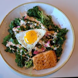 So-cal Grain Bowl - A salad featuring kale, radishes, and microgreens, topped with a fried egg and accompanied by a piece of grilled salmon.