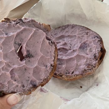 Sandy Bottom Bagels - a person holding a bagel with purple frosting - Breakfast & Brunch Near Me - Saint Simons Island, Georgia Sandy Bottom Bagels - a person holding a bagel with purple frosting - Breakfast & Brunch Near Me - Saint Simons Island, Georgia