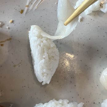 Koi Sushi - 10% fish, 90% rice. Thinnest cut of fish and dense block of rice! - A piece of sushi rice and a slice of fish are held by chopsticks on a speckled plate, with some other food remnants nearby. - Japanese Near Me - Chicago, Illinois