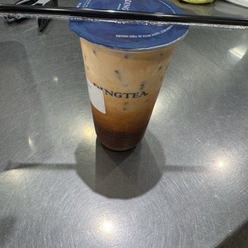 Ding Tea Tucson - A tall iced tea beverage with a blue plastic lid is placed on a metallic table, with sunglasses, a yellow cloth, and a glass of beer in the background. - Bubble Tea Near Me - Tucson, Arizona