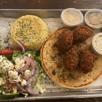 Meso Grill - Falafel plate! - A metal tray holds a meal with four falafel balls on pita bread, accompanied by a serving of rice garnished with herbs, a fresh salad with cucumber, tomato, red onion, and feta cheese, and three small containers of sauces or dressings. The presentation suggests a Middle Eastern cuisine dish. - Mediterranean Near Me - Albuquerque, New Mexico