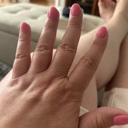 SNS Powder Gel #192 Essie Polish #1833 Loud & Proud - A close-up of a hand with pink nail polish resting on a person's leg, with a blurred background of a living room.