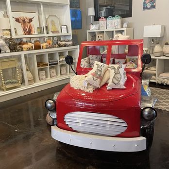 Be Here Now - No matter if you have children, or if you're a child at heart, or just love cool things... don't miss this corner! - A red children's ride-on car with bunny-themed pillows is displayed indoors, surrounded by home decor items and artwork. - Furniture Stores Near Me - Independence, Missouri