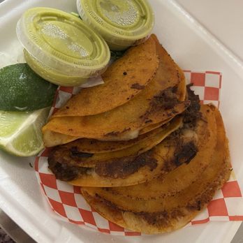 El Chivito Tortas Ahogadas - Two salsa verde cups, two slices of lime, 3 Quesabirria tacos and onions and cilantro in the plate - Mexican Near Me - San Antonio, Texas
