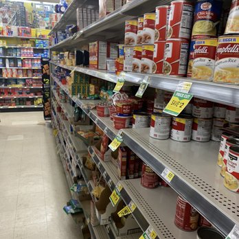 Dollar General - Well yeah it's just all in the can - A store aisle with metal shelves stocked with canned soups, including Campbell's and other brands. Price tags and promotional signs are visible, with some items marked as on sale. The background shows additional shelves with various food products, and a shopping cart is partially visible at the bottom of the image. - Grocery Near Me - Coraopolis, Pennsylvania