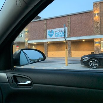 ALDI - I just visited to buy milk, black pepper and walnuts. 40 bucks later... - The image shows the exterior of a shopping center with a curbside pickup sign, taken from inside a parked vehicle. - Grocery Near Me - Timonium, Maryland