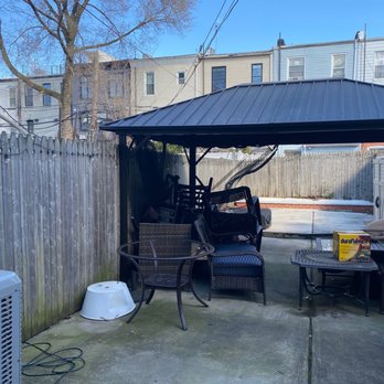 Dream Contracting - An outdoor patio area features a gazebo, various chairs, tables, and a wooden fence, with a clear blue sky overhead. - Masonry/Concrete Near Me - Brooklyn, New York