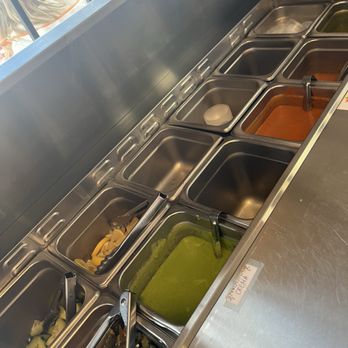 Tumerico - Salsa bar! They are all sooooo delicious! - A salsa bar with multiple stainless steel containers holding different sauces, toppings, and condiments, some with tongs and ladles. - Vegan Near Me - Tucson, Arizona