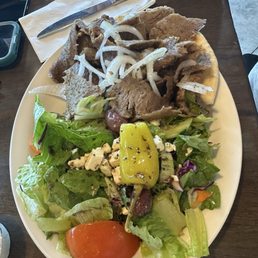 Gyro plate - A plate of Greek food featuring fried meat with onions and a side salad with vegetables, cheese, and a yellow pepper.