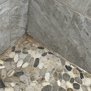 Noble Contracting Group - a corner of a shower with pebbles on the floor - General Contractors Near Me