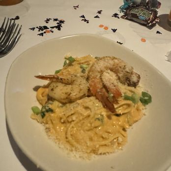 Bonefish Grill - A white plate contains seafood pasta with shrimp, scallops, and green onions in a creamy sauce. The dish is placed on a table with scattered Halloween-themed confetti, and there are drinks and candies visible in the background. - Seafood Near Me - Brookfield, Wisconsin