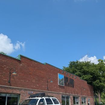 Upland Brewing - Bloomington - Front - A brick commercial building with large windows and a sign on the facade, with a white SUV parked along the street in front. - American Near Me - Bloomington, Indiana