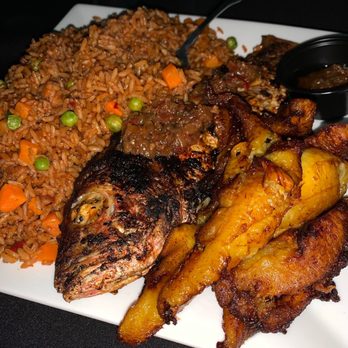 Afrique D Lounge - A plate features fried fish, seasoned rice with vegetables, fried plantains, and a small container of sauce, served on a white dish. - African Near Me - Providence, Rhode Island