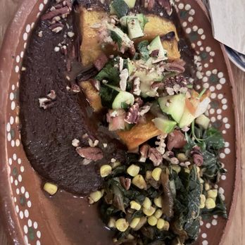 Bombera - Black mole roasted butternut squash - Roasted butternut squash with dark mole sauce, garnished with chopped cucumbers, greens, and chopped pecans, served on a decorative ceramic plate. - Mexican Near Me - Oakland, California