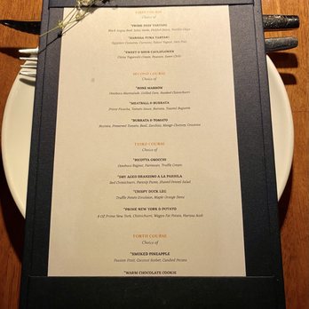 Ossobuco Miami- Steak house - Miami Spice Menu - A multi-course restaurant menu on a black-bordered folder, featuring dishes like beef tartare, tuna tartare, and various main courses, with a small flower on top. - Steakhouses Near Me - Miami, Florida