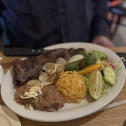 Carne Asada - A plate featuring grilled meat, rice, and a side salad with cucumbers, lime, and peppers, served at a Mexican restaurant.