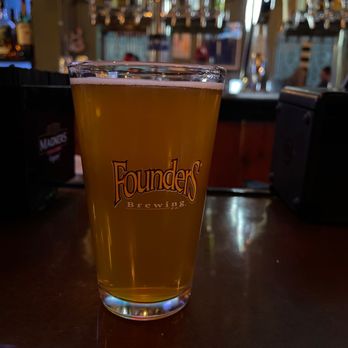 Villa Capri - Chilling at the bar - A pint glass filled with beer featuring the Founders Brewing logo is on a bar counter, with a blurred bar background including taps and bottles. - Pizza Near Me - Doylestown, Pennsylvania