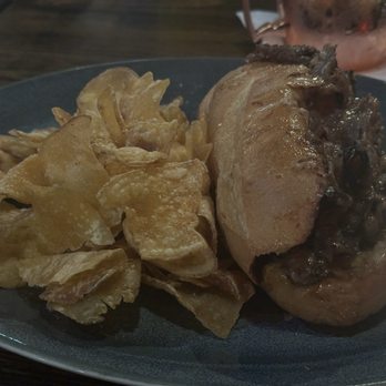 Bosscat Kitchen & Libations - A photograph shows a plate with a stuffed chicken breast topped with a dark sauce and a side of potato chips. The dish is served on a dark plate, and the setting appears to be a restaurant environment, likely Bosscat Kitchen & Libations in Orange, California. - Bars Near Me - Orange, California