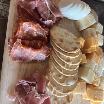 Jackdaw - Charcuterie. Not as pretty as the norm. But still good. I would ask what's in it for the night before you order. - The image shows a wooden board with an assortment of food items including slices of cured meats such as prosciutto and salami, several slices of different cheeses, and round bread slices. The items are arranged in a way typical for a charcuterie platter, with the meats and cheeses placed in separate sections. The background suggests a rustic setting, possibly a kitchen or dining area. - Irish Near Me - Fort Worth, Texas