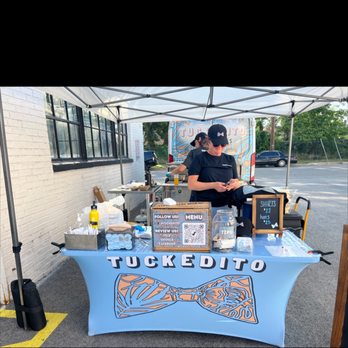 Tuckedito Taquitos - a man standing behind a table - Food Trucks Near Me Tuckedito Taquitos - a man standing behind a table - Food Trucks Near Me