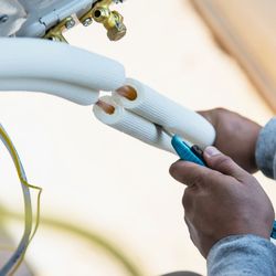 Buckhorn Heating & Air Conditioning - Technician cutting insulated copper refrigerant lines during HVAC installation, preparing piping connections for an air condi...