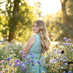 J Corchero Portraits - Senior girl looking over her shoulder smiling while standing in a garden full of flowers.