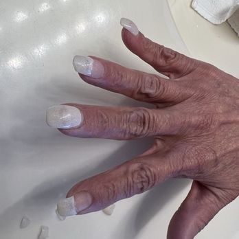 Flashy Nails - lol - A hand with long, square-shaped acrylic nails painted with a glittery white polish is resting on a white surface, with some nail tips and debris nearby. - Nail Salons Near Me - Albuquerque, New Mexico