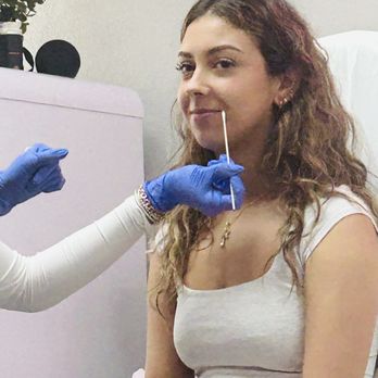 Aesthetic Lab - A woman with curly hair is seated while a healthcare worker in blue gloves administers a nasal swab test. - Medical Spas Near Me - Modesto, California