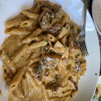 Pasta E Basta - Sweet and spicy cream sauce with breaded chicken with penne! - A plate of penne pasta coated in a creamy, spicy sauce with pieces of breaded chicken and garnished with chopped herbs. The dish is served on a white oval plate, with a fork placed on the right side. The background includes a granite countertop and a small dish with remnants of food. - Italian Near Me - Amherst, Massachusetts