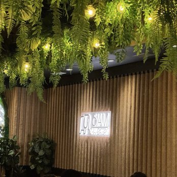 Siam Thai Eatery - Indoor space with a ceiling decorated with hanging green plants and string lights, and a wooden wall with a neon sign. - Thai Near Me - Chicago, Illinois
