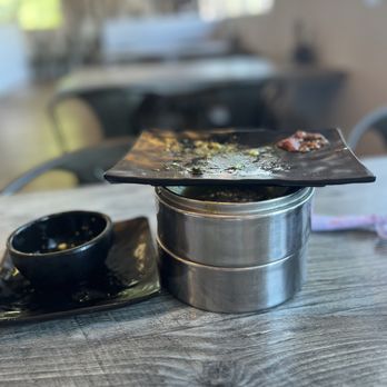 IT DIMSUM - Licked the plates clean! - A black plate with remnants of food is stacked on a metal container, accompanied by a small black bowl on a black tray, on a wooden table. - Dim Sum Near Me - Albuquerque, New Mexico