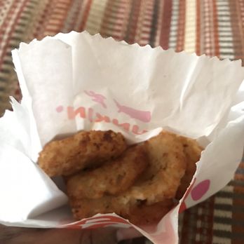 Dunkin' - Hash Browns - The image shows three pieces of fried chicken with a crispy, golden-brown coating inside a crumpled white paper bag. The bag has some red text partially visible. The background features a fabric surface with a multicolored, striped pattern. The photo is taken from a top-down perspective, focusing on the chicken and the paper bag. - Donuts Near Me - Fairfax, Virginia