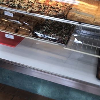 The Bread Boss - A glass display case at The Bread Boss bakery in Johnston, RI, contains several pizzas, pastries, and baked goods. The pizzas are topped with ingredients like vegetables and cheese, while other baked items include calzones and pastries. Some items are labeled with small signs, and the case is illuminated from above. The bakery offers a variety of freshly baked products, including zeppole and cookies, and is open daily. - Pizza Near Me - Johnston, Rhode Island